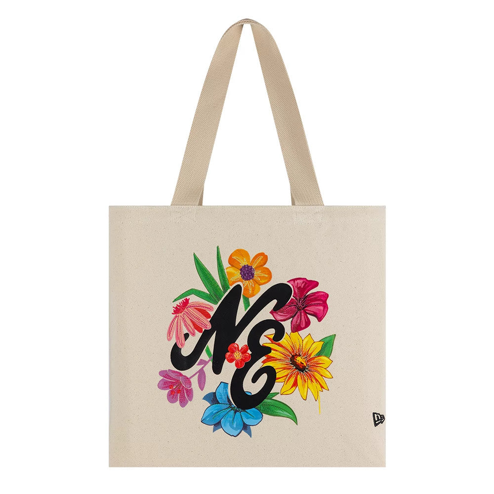 New Era Graphic Light Beige Tote Bag, front view displaying a floral design surrounding black letters NE, two handles emerging from the top, and a small embroidered New Era logo near the bottom right corner.