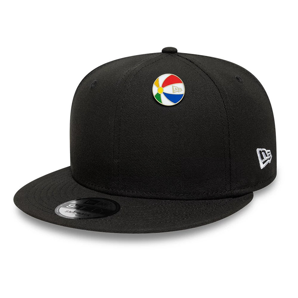 New Era Beachball Gold Pin Badge, front view on a black cap featuring a colourful round pin with segments of red, blue, green, and yellow, a debossed New Era logo on the pin, and an embroidered white New Era logo on the side.