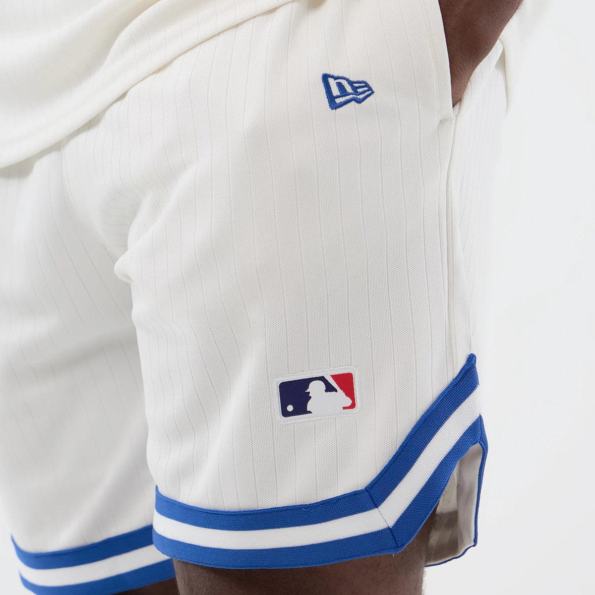New Era LA Dodgers MLB Arch Open White Oversized Shorts, side view showing the white pinstriped design, blue embroidered New Era logo near the waistband, MLB Batterman logo above the hem, and blue and white striped trim at the bottom edge.