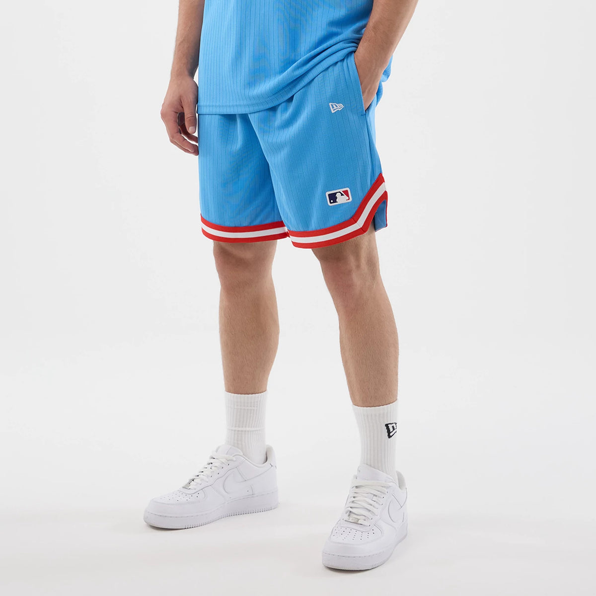 New Era New York Yankees MLB Arch Pastel Blue Oversized Shorts, front view on-model with a matching top, showcasing embroidered New Era flag logo on the left thigh, MLB logo near the hem, and red and white striped trim.