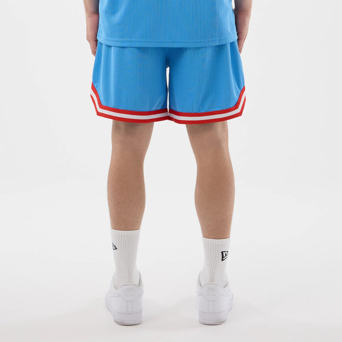 New Era New York Yankees MLB Arch Pastel Blue Oversized Shorts, back view on a model showing the light blue shorts with red and white striped trim at the hem, paired with a matching top, white socks, and white trainers.