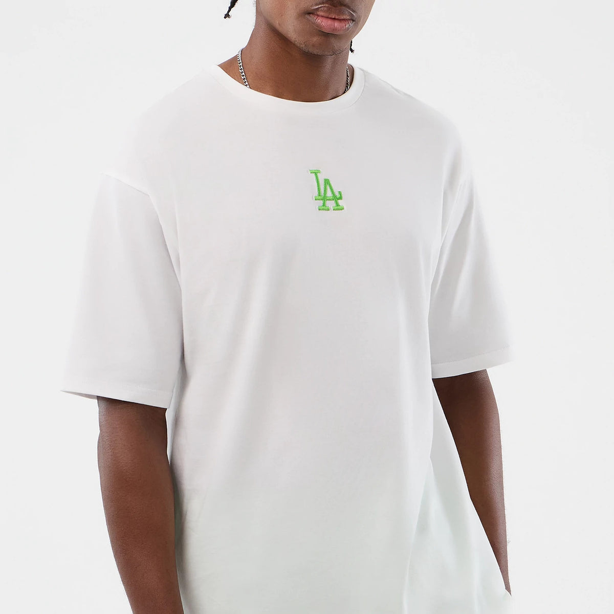 New Era LA Dodgers MLB League Essential White Oversized T-Shirt, front view on a model showing a green embroidered LA logo centred on the chest, with short sleeves and a wide crew neck, creating a relaxed, streetwear-inspired style.