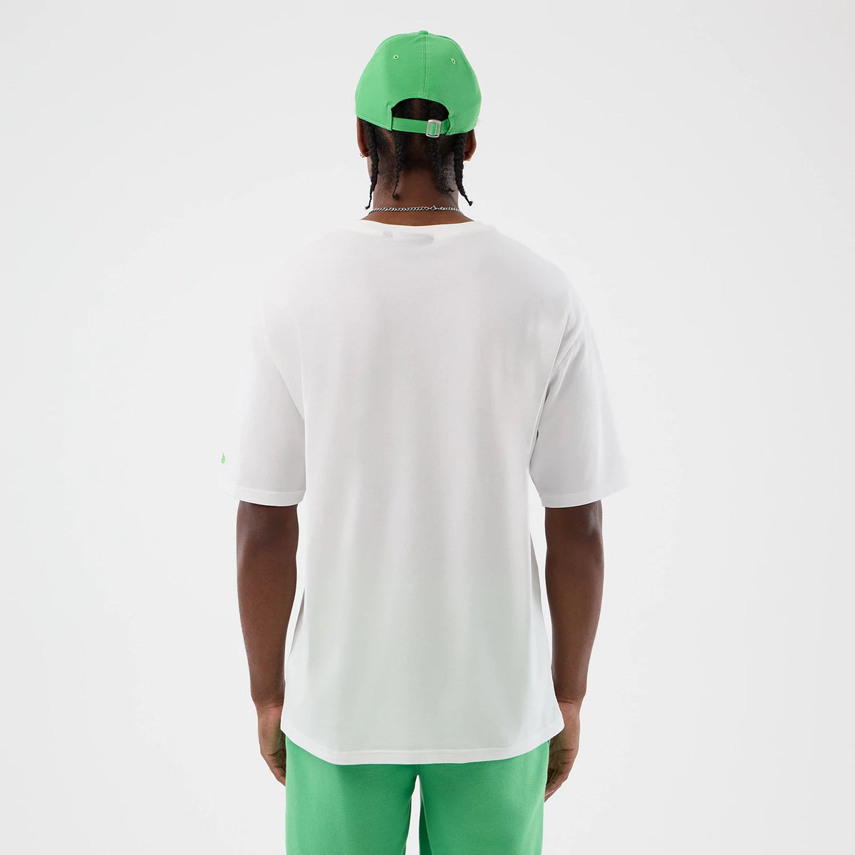New Era LA Dodgers MLB League Essential White Oversized T-Shirt, back view on a model styled with green shorts and a cap, showing the plain white fabric with a New Era logo embroidered on the left sleeve.