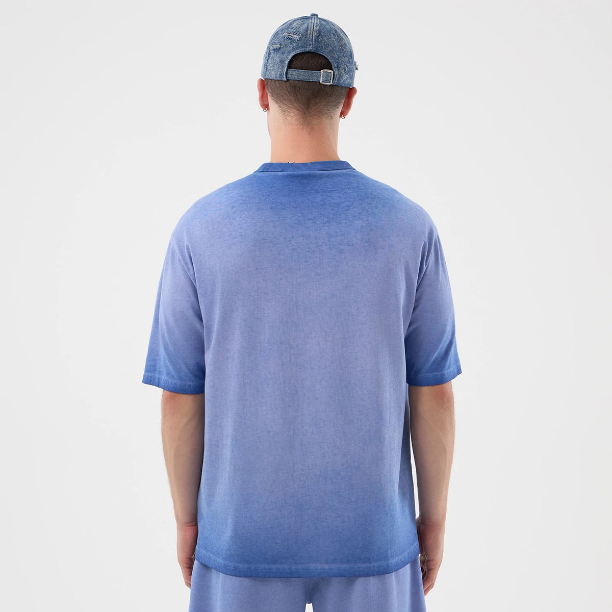 New Era LA Dodgers MLB Washed Logo Pastel Blue T-Shirt, back view on-model showcasing the soft fading of the pastel blue fabric towards the hem and sleeves, worn with matching blue shorts and a blue cap featuring an embroidered patch at the back.