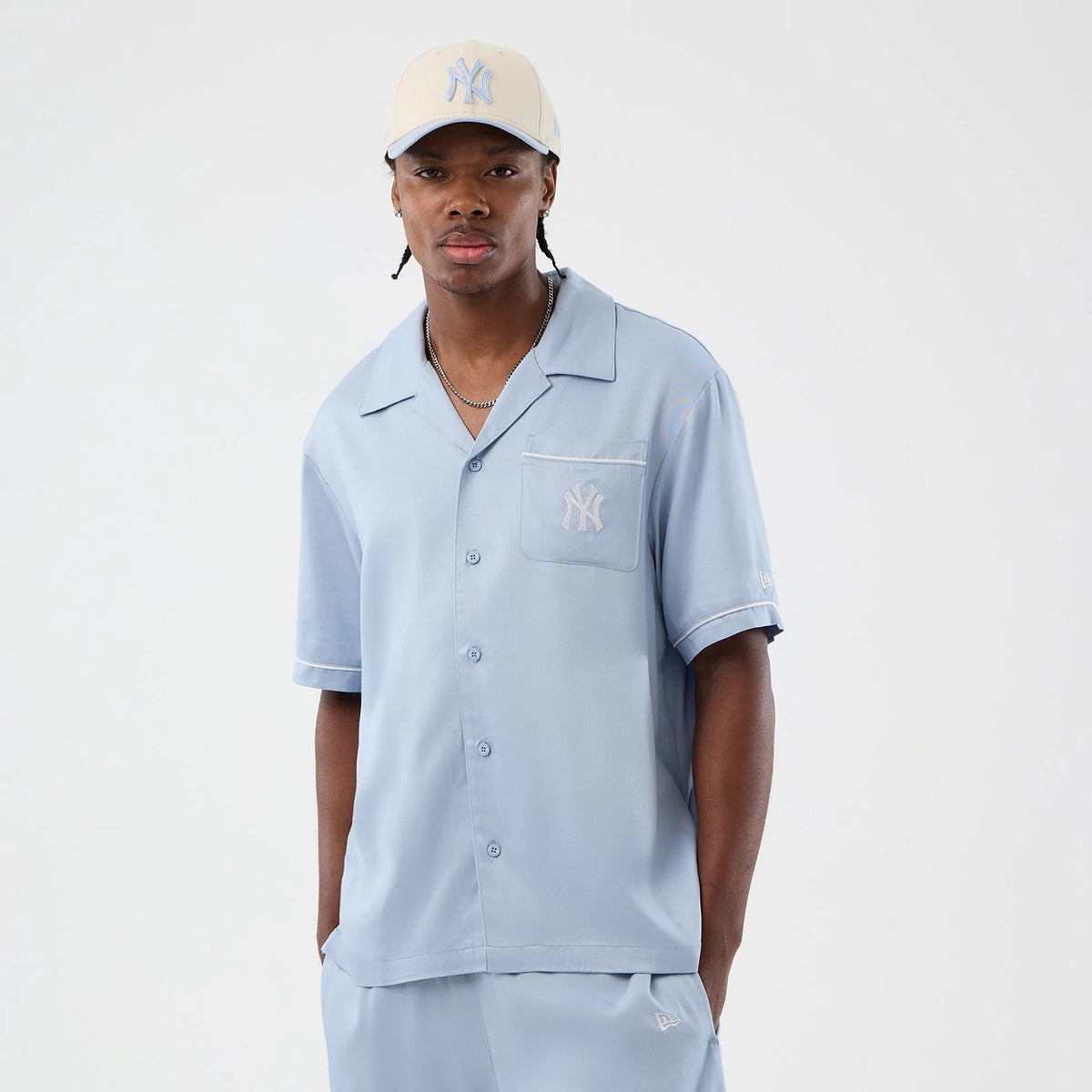 New Era New York Yankees MLB Graphic Revere Pastel Blue Short Sleeve Shirt, front view on a model wearing a matching pastel cap, featuring the Yankees logo embroidered on the chest pocket, button-down front, and folded collar.