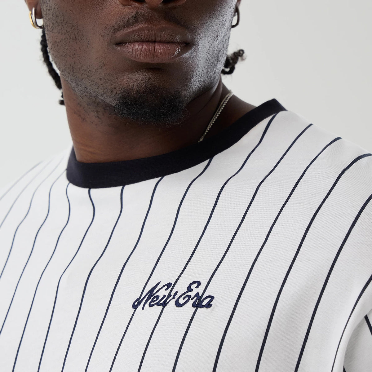 New Era Pinstripe Open White Oversized T-Shirt, three-quarter view showing the vertical black pinstripes, a black crew neckline, and an embroidered New Era logo in black script on the left chest.