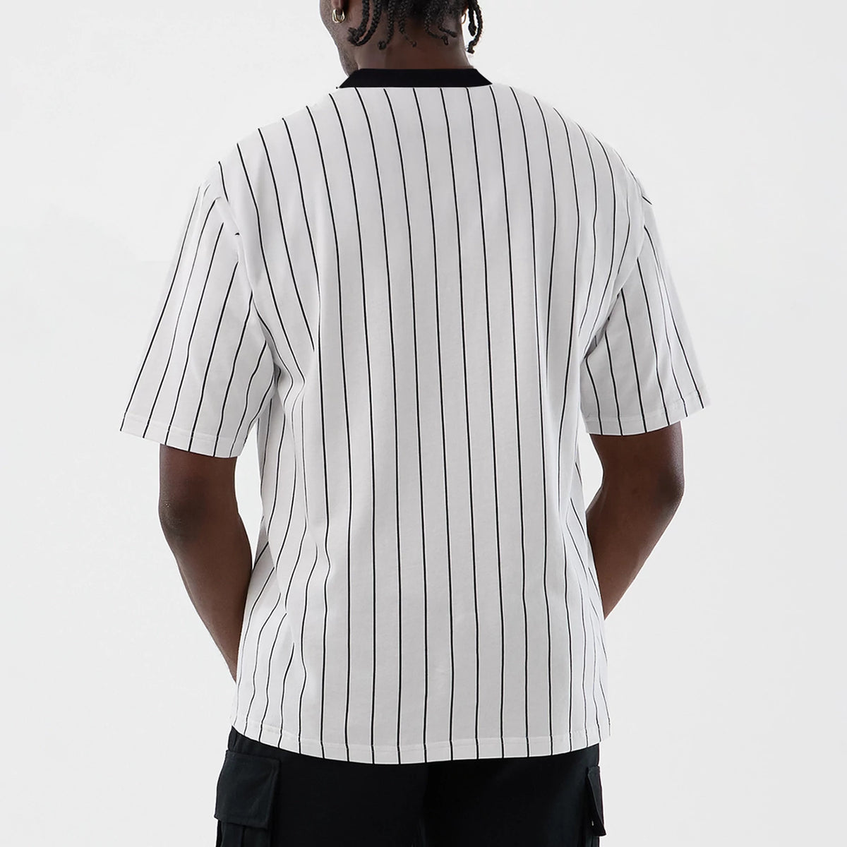 New Era Pinstripe Open White Oversized T-Shirt, back view on a model showcasing the vertical black pinstripes, a plain black round collar, and short sleeves that fall loosely to the arm.