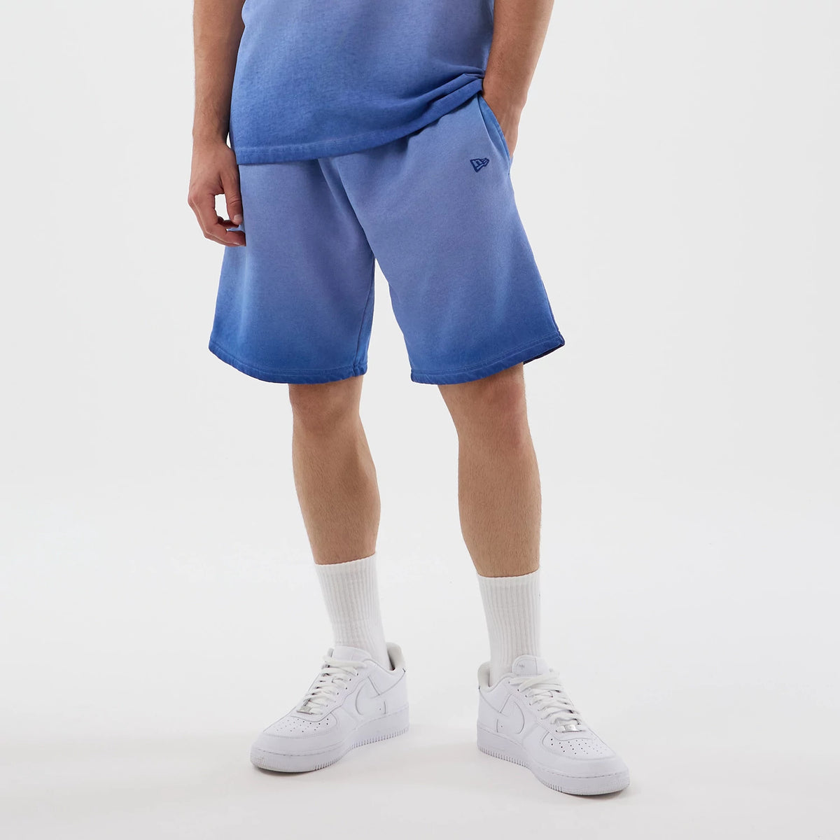 New Era LA Dodgers MLB Washed Logo Pastel Blue Shorts, front view on-model showing the gradient pastel blue colour with darker hems, the New Era embroidered logo on the left leg, styled with a matching top and white trainers.