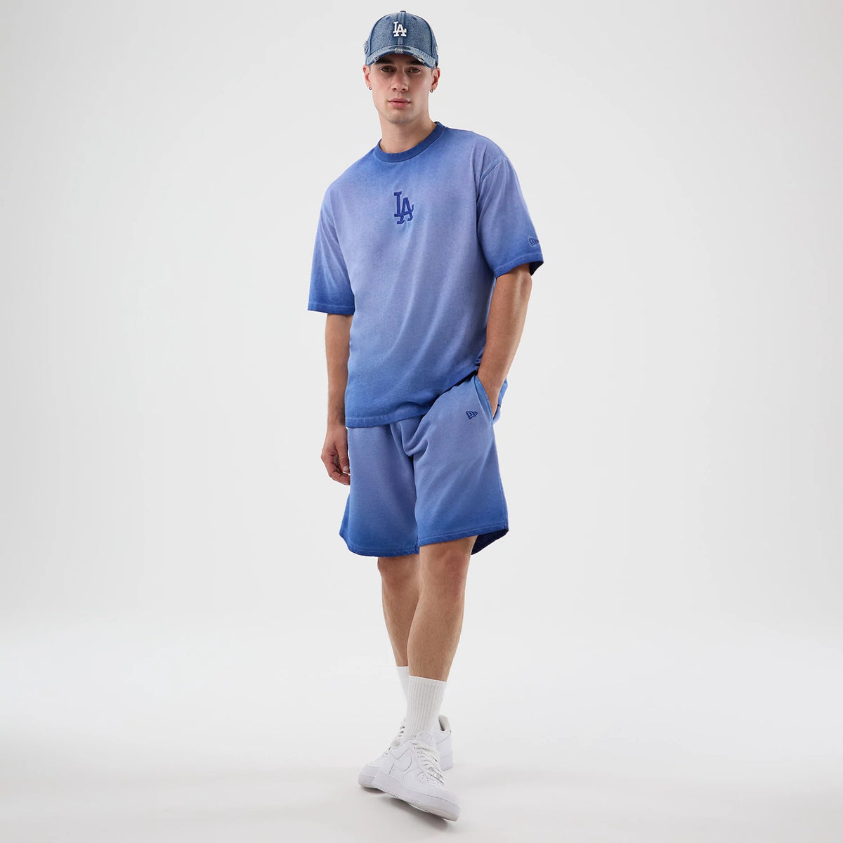 New Era LA Dodgers MLB Washed Logo Pastel Blue Shorts, on-model front view highlighting the pastel blue hue and relaxed fit, with an embroidered New Era logo on the left leg and paired with a matching T-shirt and cap for a coordinated look.