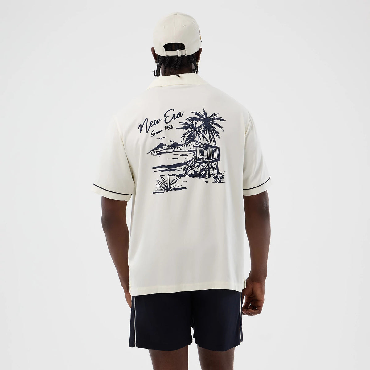 New Era Graphic Revere Open White Short Sleeve Shirt, back view on a model showcasing a black and white tropical scene graphic with palm trees and a beach house, New Era script above, and contrasting black trim on the sleeves.
