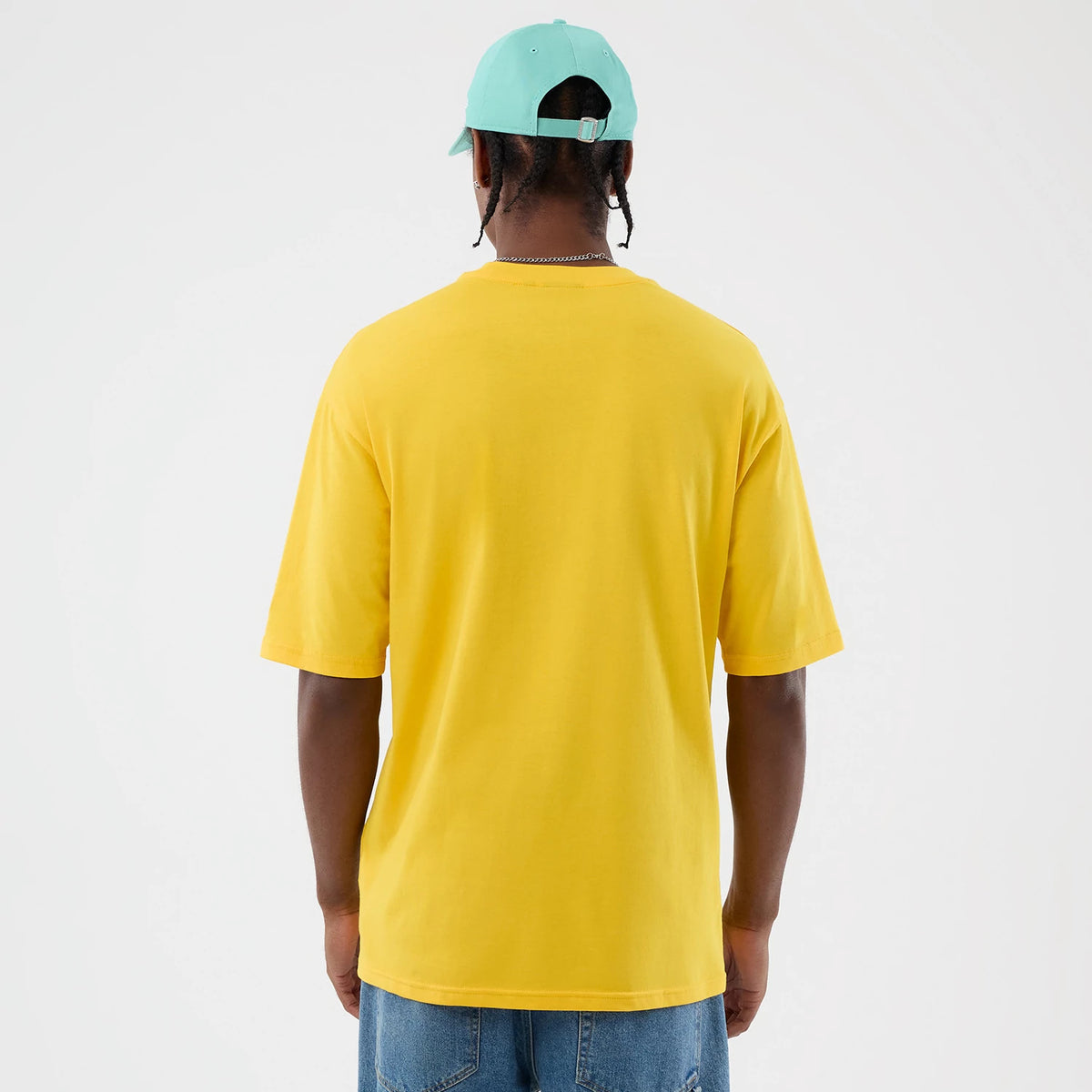 New Era Alligator Character Graphic Yellow T-Shirt, back view on a model wearing a turquoise cap and denim jeans, showcasing the plain yellow back of the shirt with short sleeves and a relaxed fit.