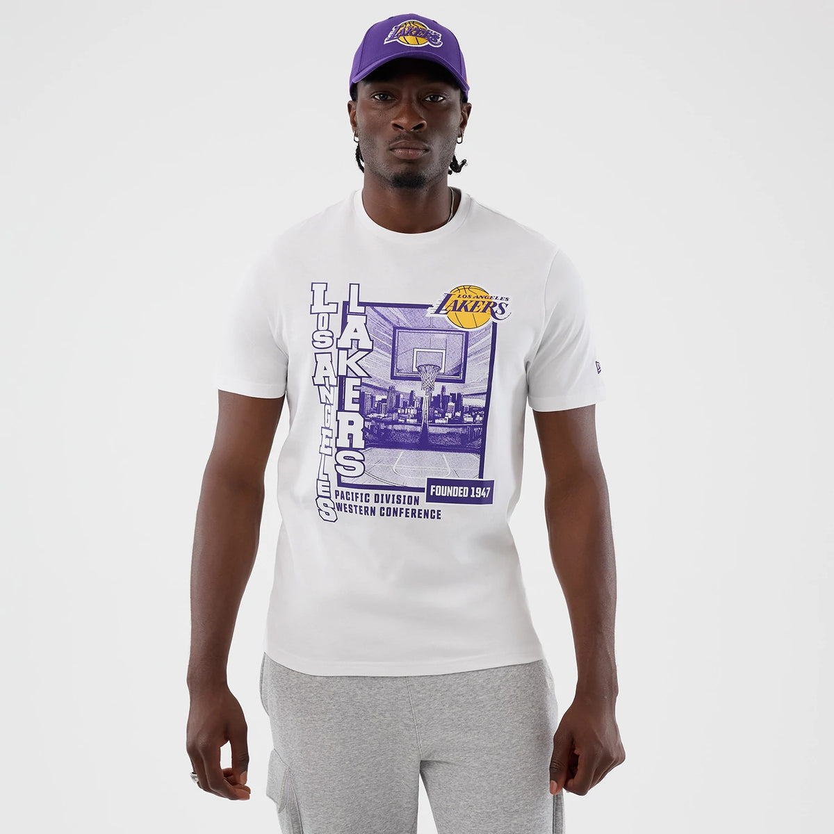 New Era LA Lakers NBA Graphic White T-Shirt, front view on-model showing a purple and black graphic with a basketball hoop and city skyline, large Lakers text down the left side, and a Lakers logo on the chest.