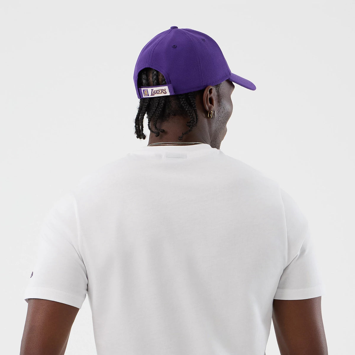 New Era LA Lakers NBA Graphic White T-Shirt, back view on a model styled with a purple cap, showing a plain white back with short sleeves, accented by a purple Lakers logo on the back strap of the cap positioned above the neck.
