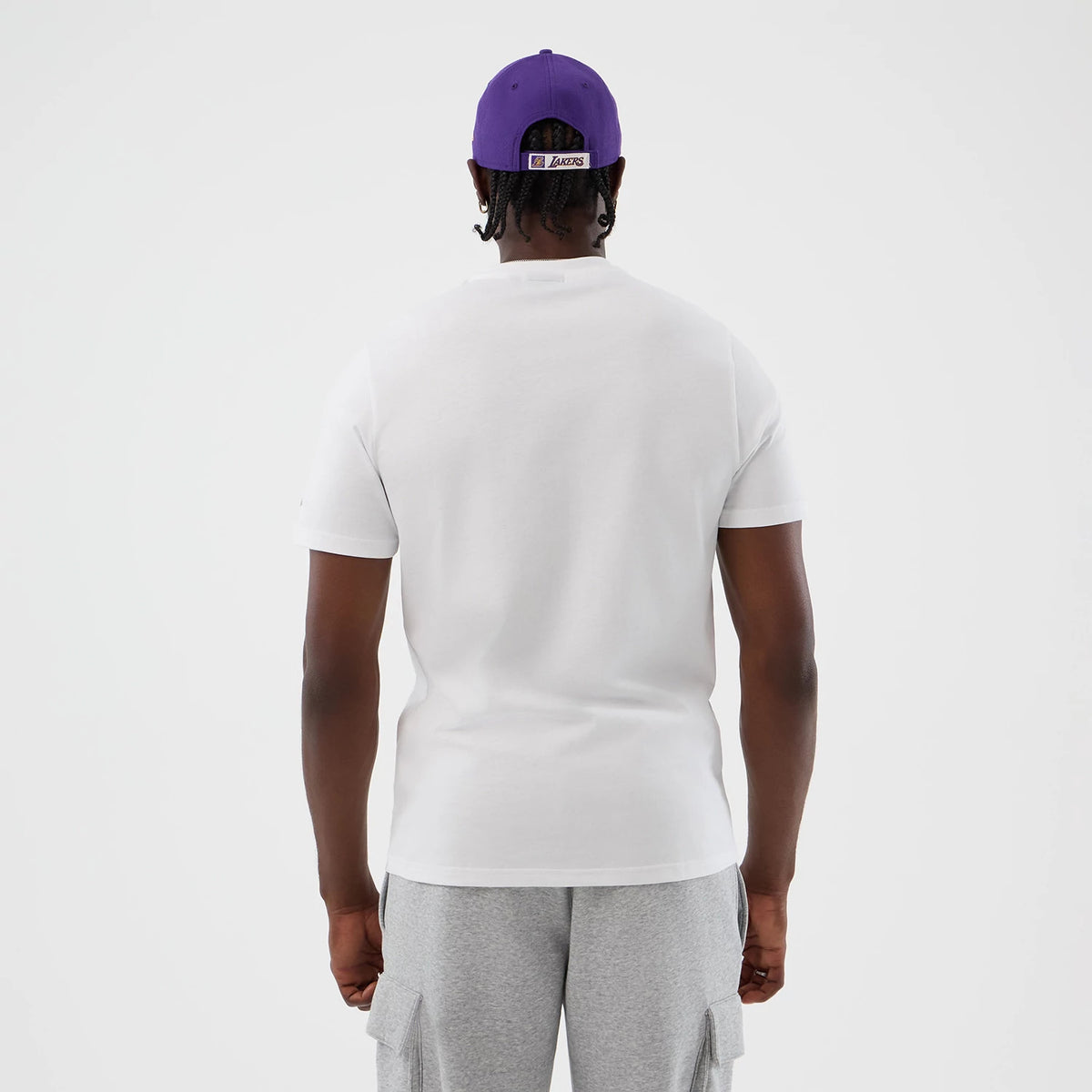 New Era LA Lakers NBA Graphic White T-Shirt, back view on a model with a purple cap, showing the plain white back of the shirt, short sleeves and a fitted cut, paired with light grey cargo shorts for a casual look.