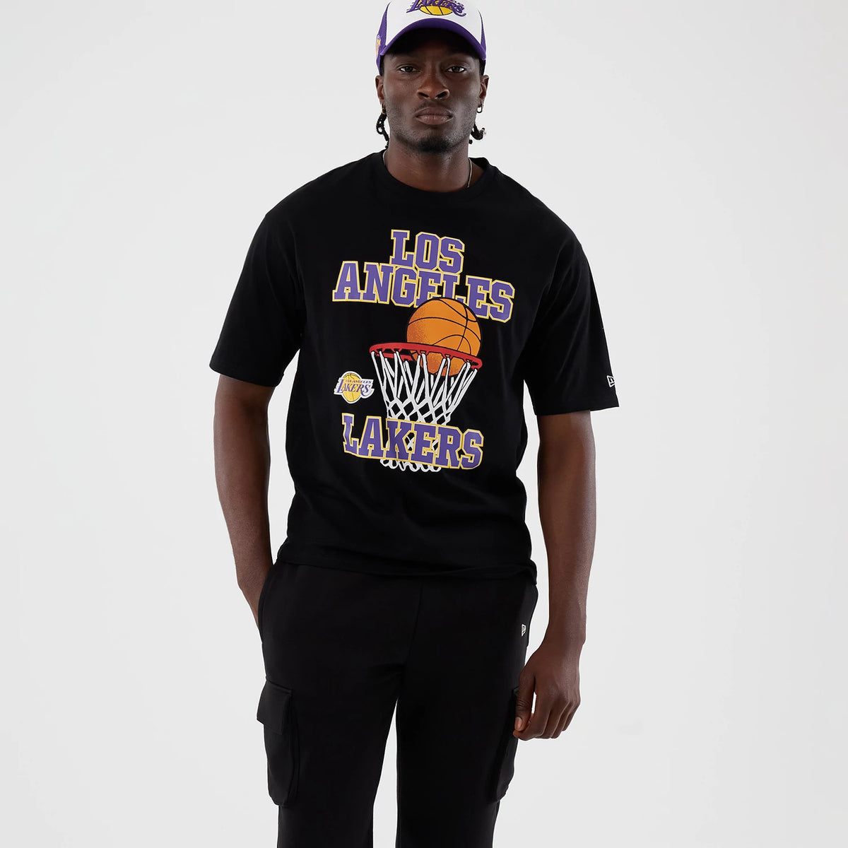 New Era LA Lakers NBA Basket Made Black Oversized T-Shirt, front view on a model styled with a matching cap, featuring a basketball graphic going through a net, large Los Angeles Lakers lettering across the chest.