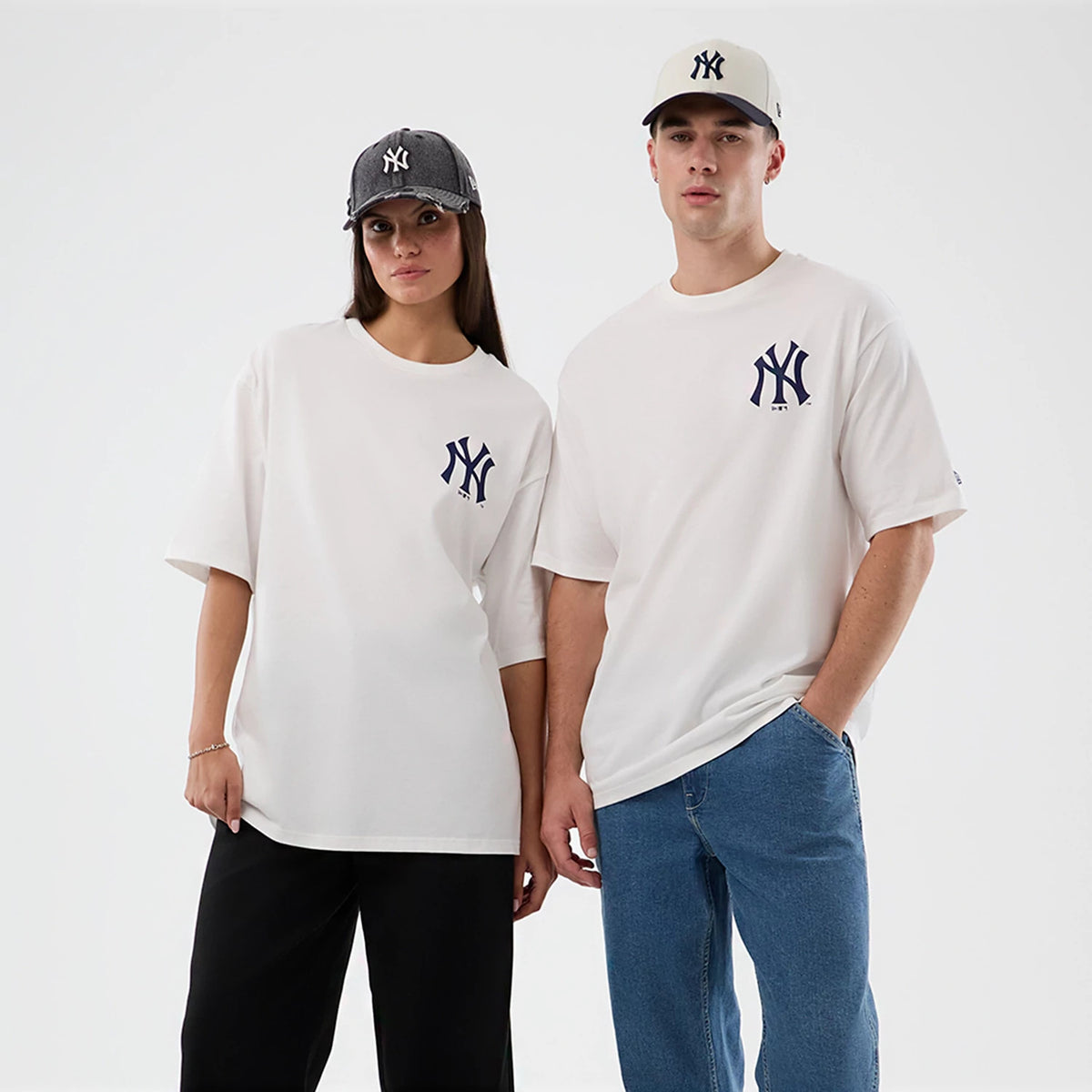 New Era New York Yankees MLB Cap Graphic White Oversized T-Shirt, front view on-model showing the large navy embroidered NY logo on the left chest, styled with a grey cap on the left model and a white cap on the right model.