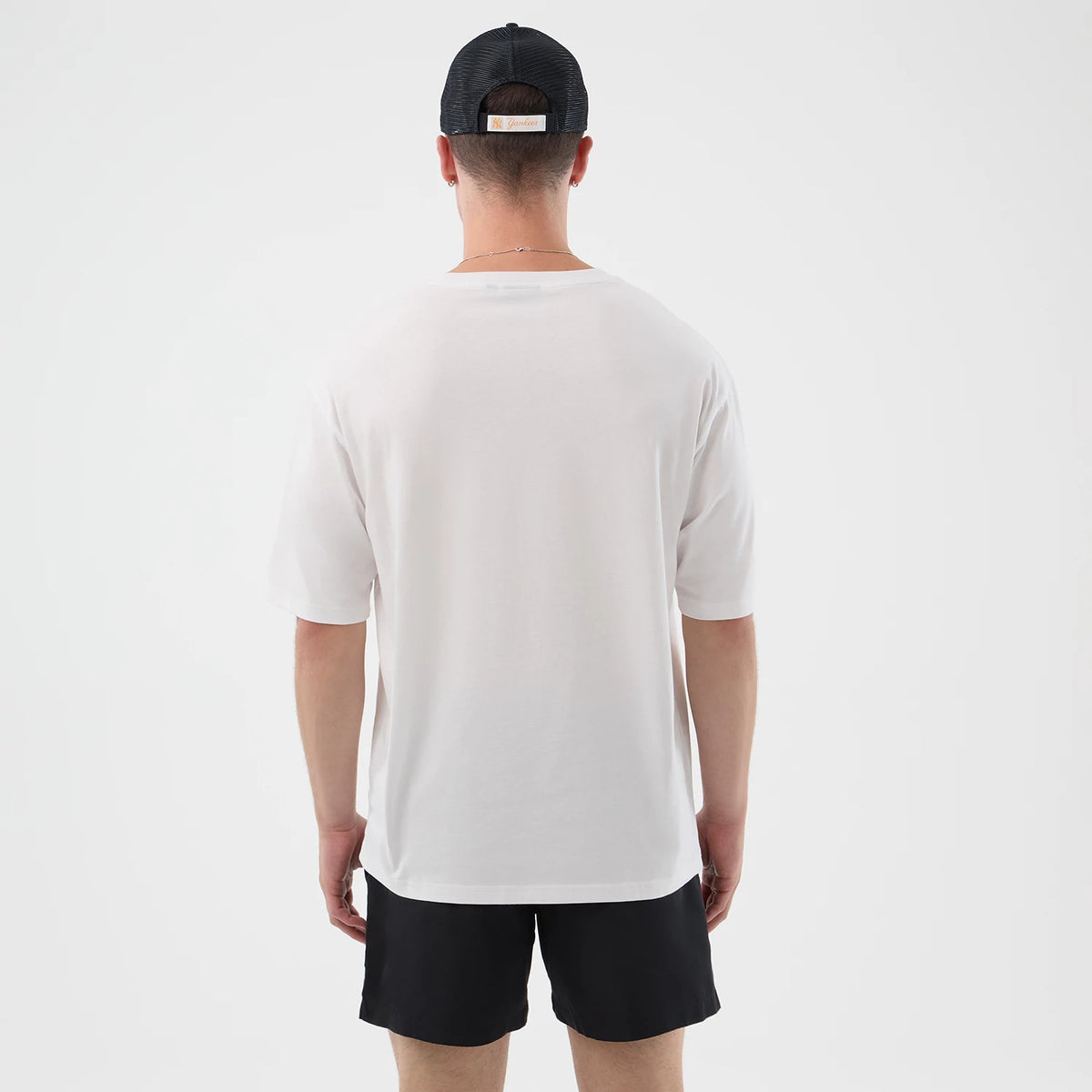 New Era Death Moth Graphic White Oversized T-Shirt, back view on a model wearing black shorts and a cap, showing the plain white fabric with no graphics or text, highlighting the relaxed oversized fit and short sleeves.