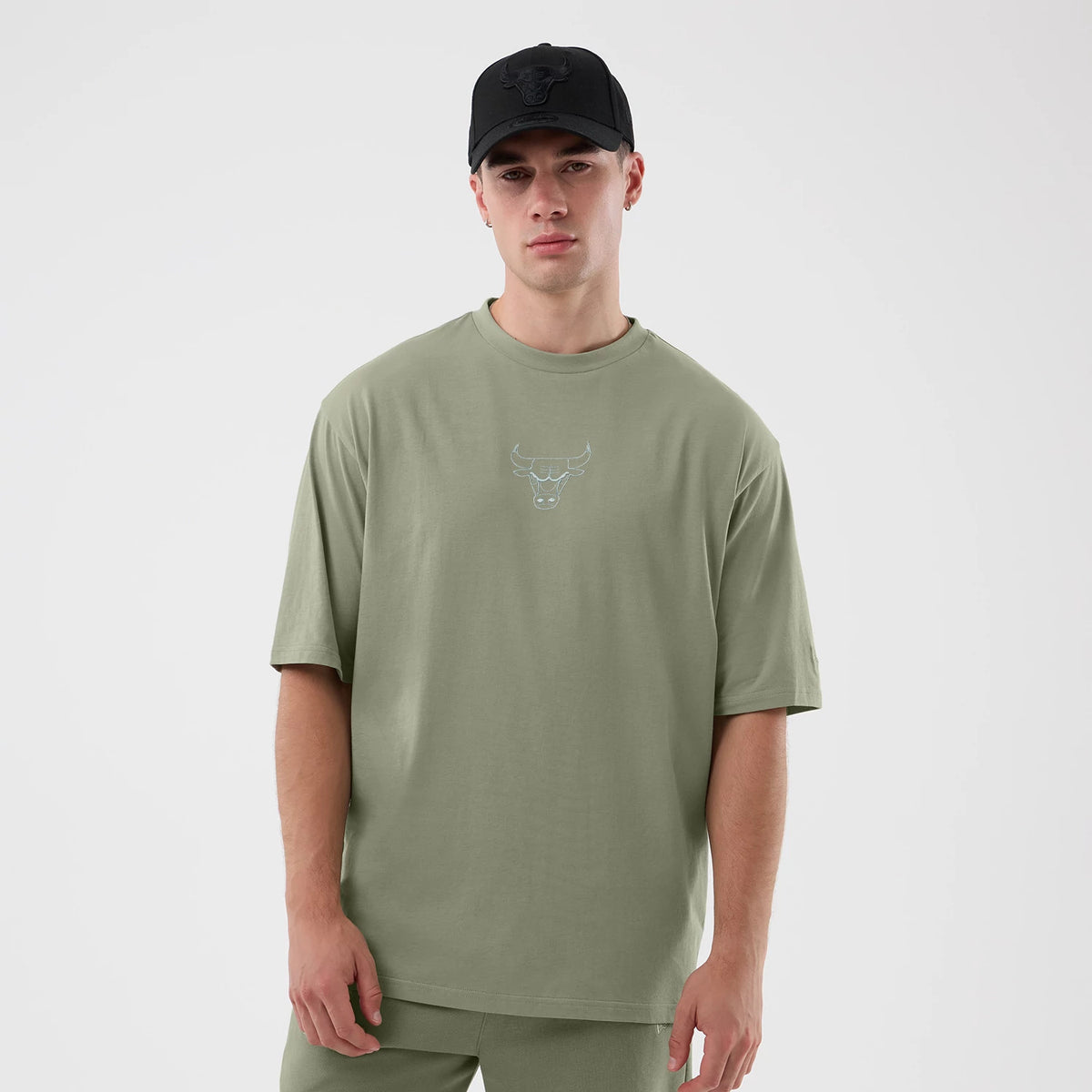 New Era Chicago Bulls NBA League Essential Pastel Green Oversized T-Shirt, front view on a model paired with a black cap, displaying a outline of the Bulls logo printed in the centre of the chest, with loose-fitting sleeves.