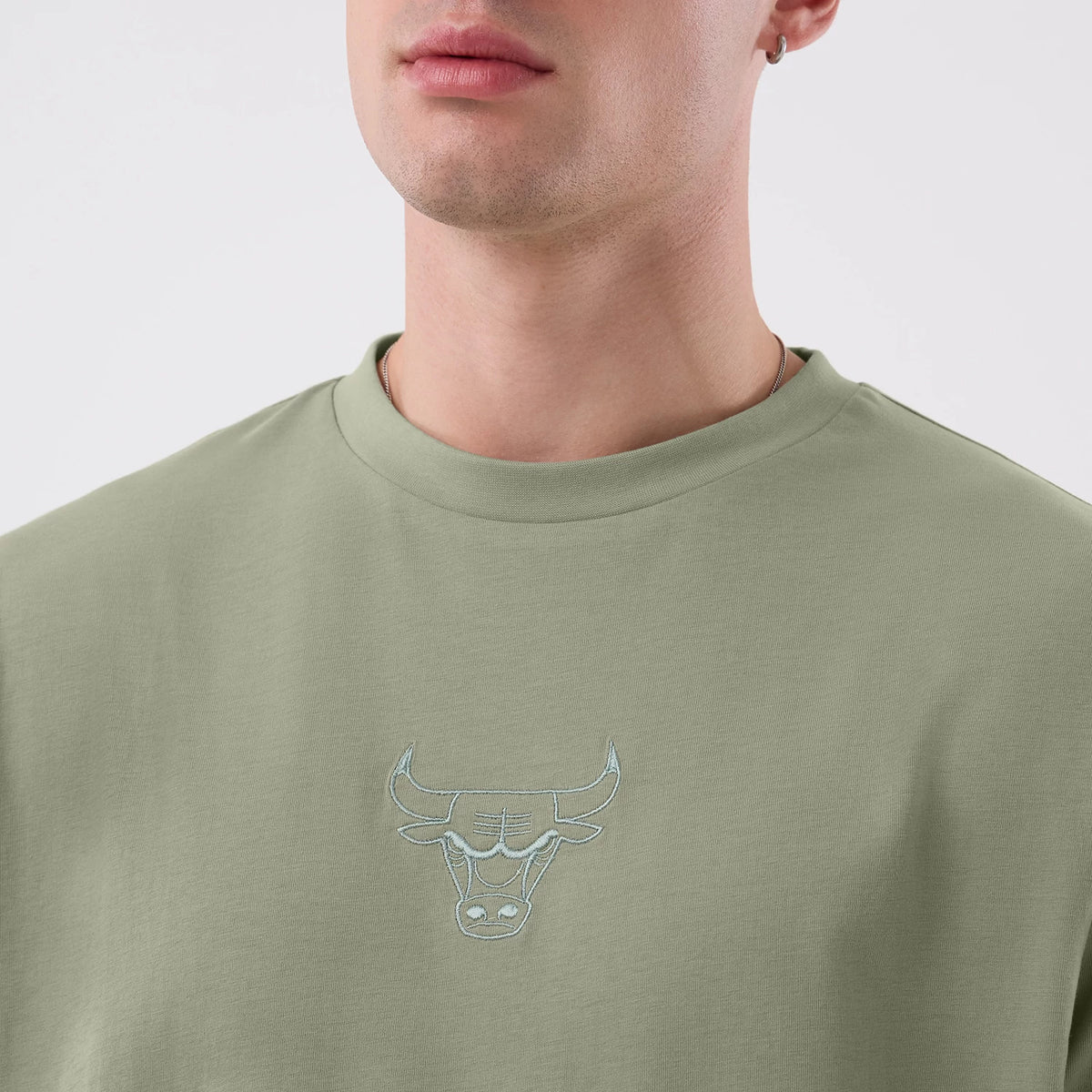 New Era Chicago Bulls NBA League Essential Pastel Green Oversized T-Shirt, front view on a model, highlighting a pastel green design with an embroidered bull logo at the centre of the chest and a relaxed, oversized fit around the neckline.