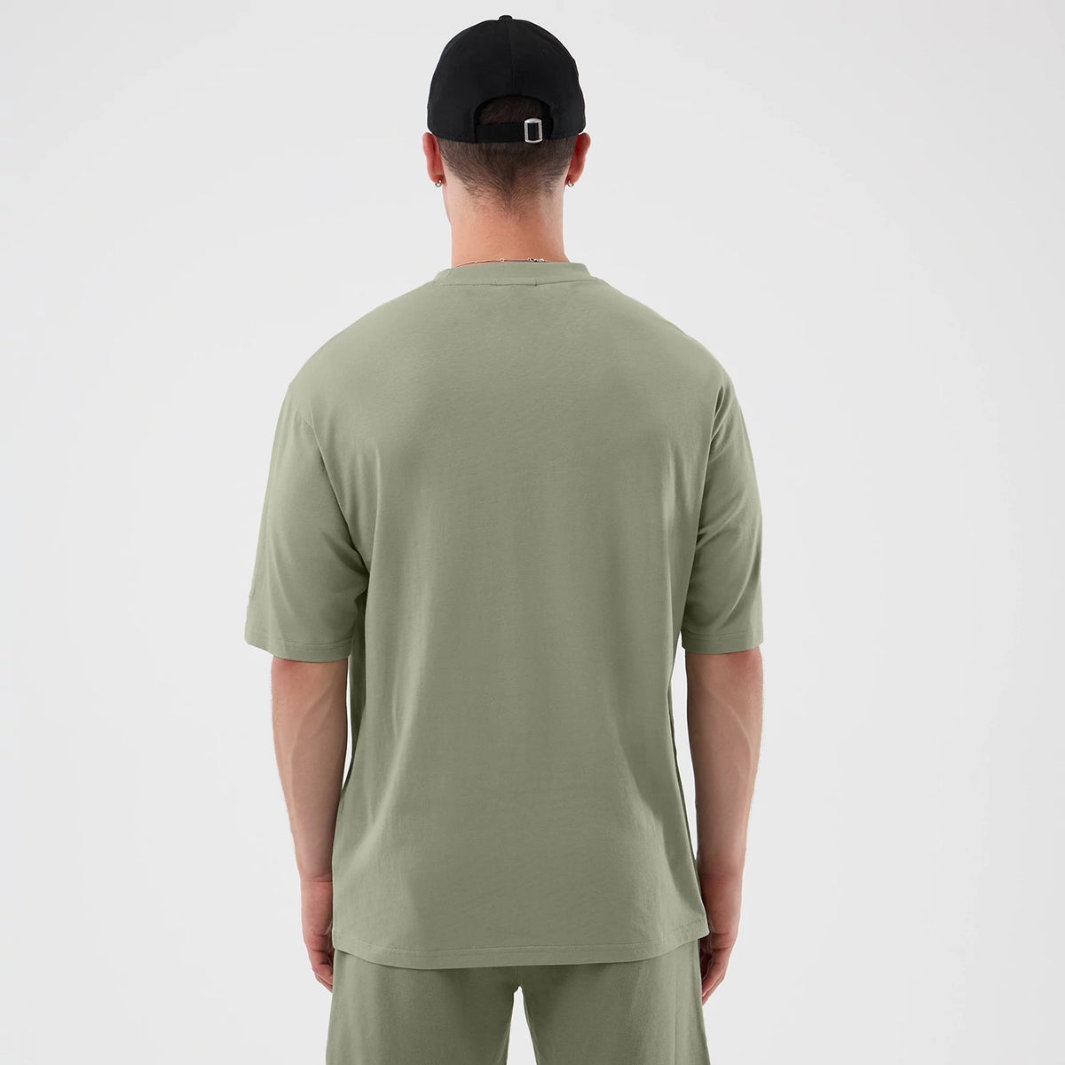 New Era Chicago Bulls NBA League Essential Pastel Green Oversized T-Shirt, back view on a model with a black cap, showcasing the plain pastel green fabric extending to mid-thigh, with short sleeves and a relaxed fit, no graphics or logos.
