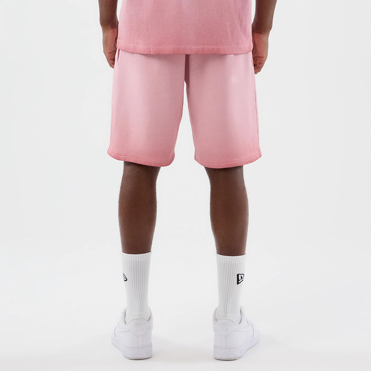 New Era New York Yankees MLB Washed Logo Pastel Pink Shorts, back view on a model showing the pastel pink fabric with a loose fit, hem reaching just above the knees, and styled with white socks bearing an embroidered New Era logo and white trainers.