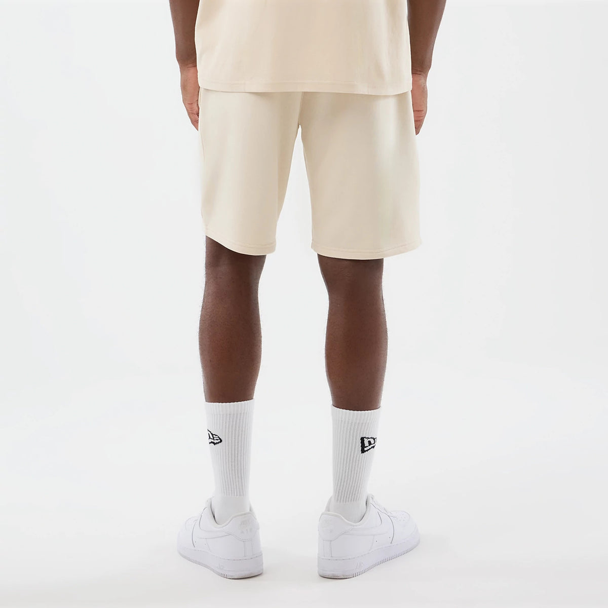 New Era Chicago Bulls NBA Core Plus Light Beige Shorts, back view on a model showing the light beige colour extending across the back, plain design with no graphics, ending just above the knee and worn with white socks and trainers.
