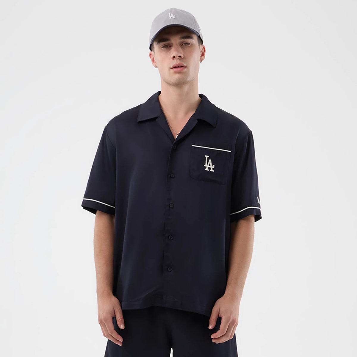 New Era LA Dodgers MLB Graphic Revere Navy Short Sleeve Shirt, front view on a model with off-white piping along the pocket and sleeves, featuring an embroidered white LA logo on the chest pocket beneath a notched collar.