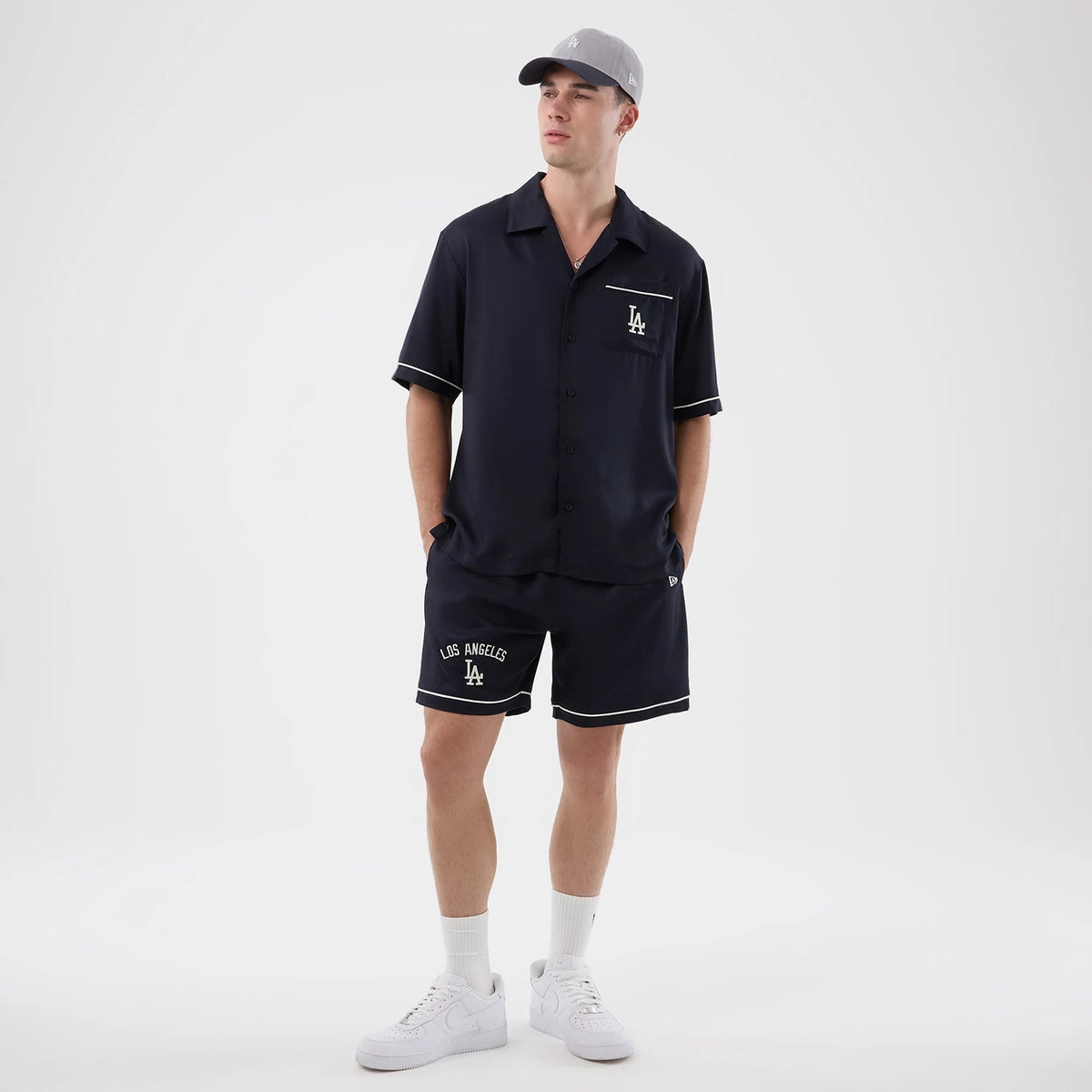 New Era LA Dodgers MLB Graphic Revere Navy Short Sleeve Shirt, front view on a model styled with matching navy shorts featuring white LA Dodgers logos on the chest pocket and left leg, along with white piping details on the hems.