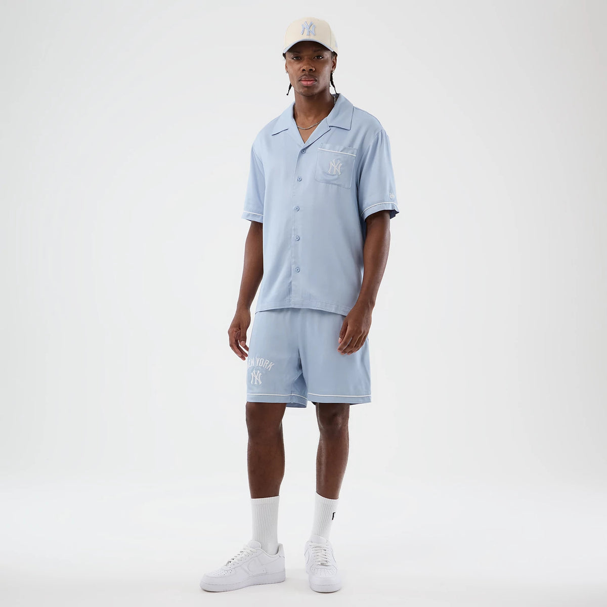 New Era New York Yankees MLB Woven Pastel Blue Shorts, front view on a model styled with a matching shirt and cap, featuring white embroidered NY logo on the left leg, New York lettering above, and a relaxed fit with a waistband.