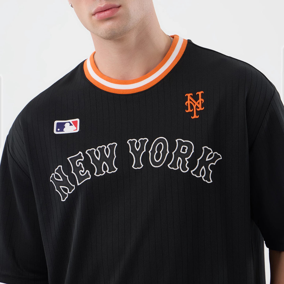 New Era New York Mets MLB Arch Black Oversized T-Shirt, front view showing embroidered New York lettering across the chest, a small orange Mets logo on the left chest, and an MLB logo patch above the contrasting orange and white striped collar.