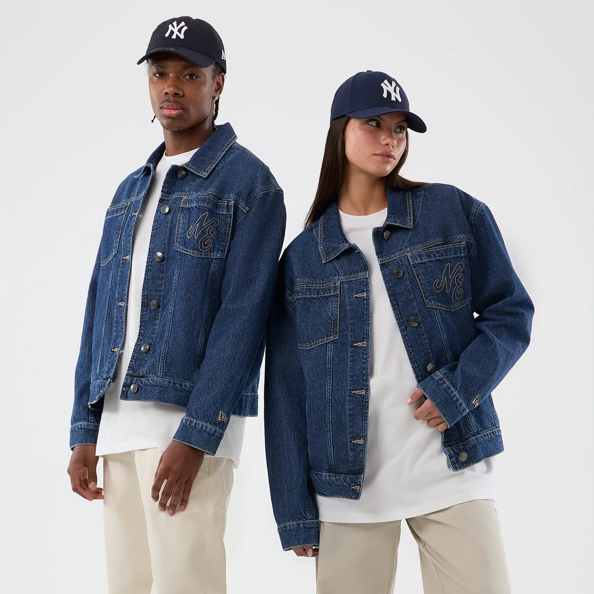 New Era Script Denim Dark Blue Jacket, on-model front view showing the embroidered NE logo on the left chest pocket, classic button-down style with stitching, and paired with a white shirt and light trousers, wearing a New York Yankees cap.