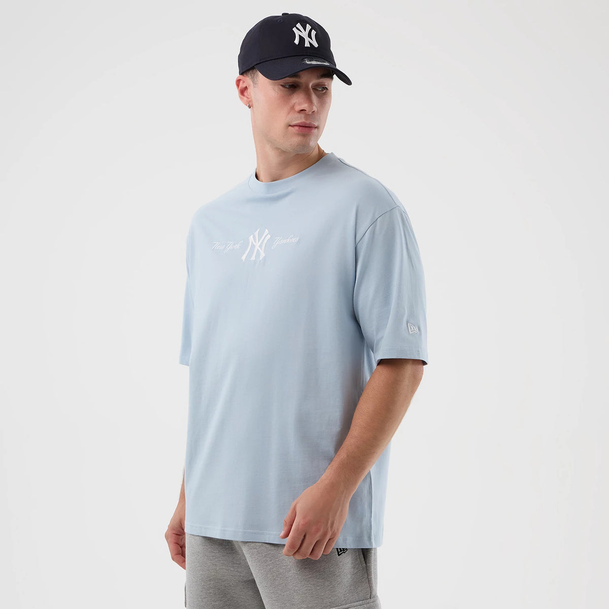New Era New York Yankees MLB Script Pastel Blue Oversized T-Shirt, front view on a model wearing a dark cap, a white embroidered New York Yankees logo across the chest and a embroidered New Era logo on the left sleeve.