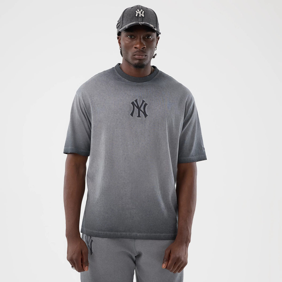 New Era New York Yankees MLB Washed Logo Black T-Shirt, front view worn by a model, showcasing the washed grey tee with a large dark grey embroidered Yankees logo centred on the chest, short sleeves, and paired with matching trousers.
