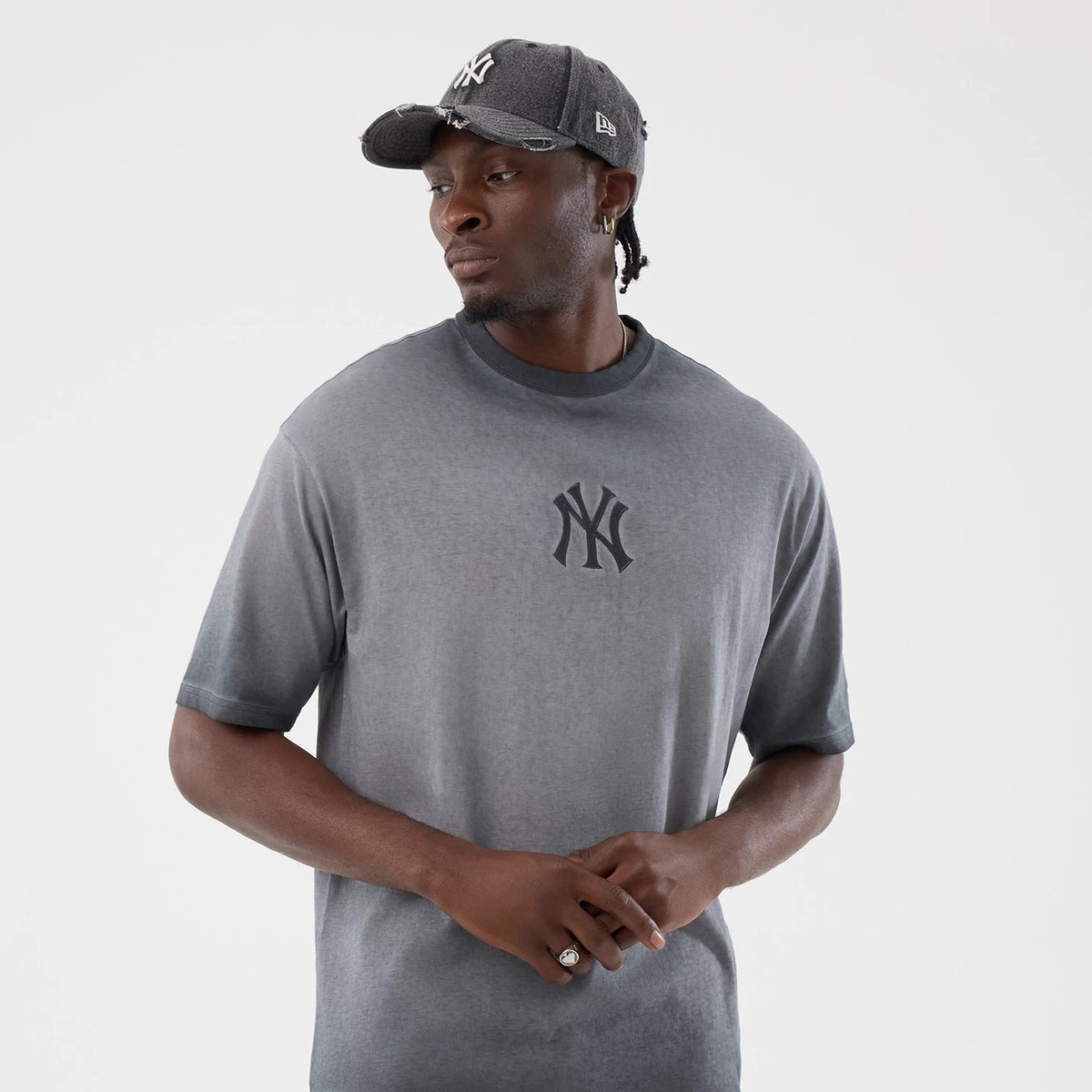 New Era New York Yankees MLB Washed Logo Black T-Shirt, front view on-model highlighting the faded black hue with an embroidered Yankees logo centred on the chest, paired with a grey cap featuring a white embroidered New Era flag on the side.
