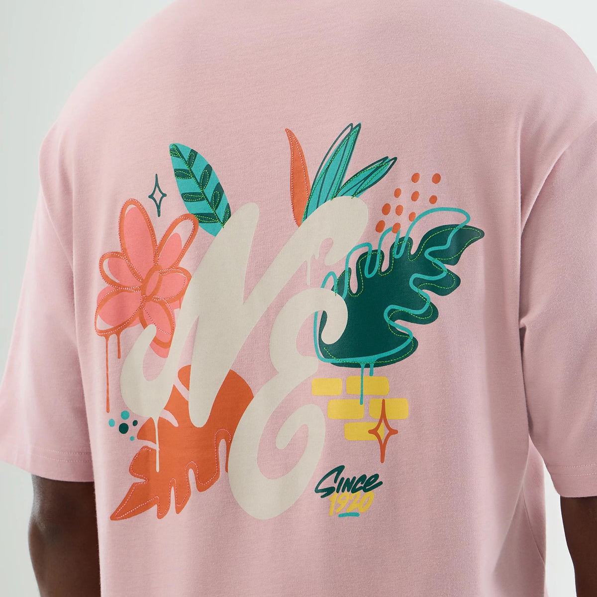 New Era Floral Graphic Pastel Pink Oversized T-Shirt, back view showing a floral graphic with stylised NE lettering, large green and orange leaves, pink and orange flower motifs, and 'Since 1920' text printed at the bottom.