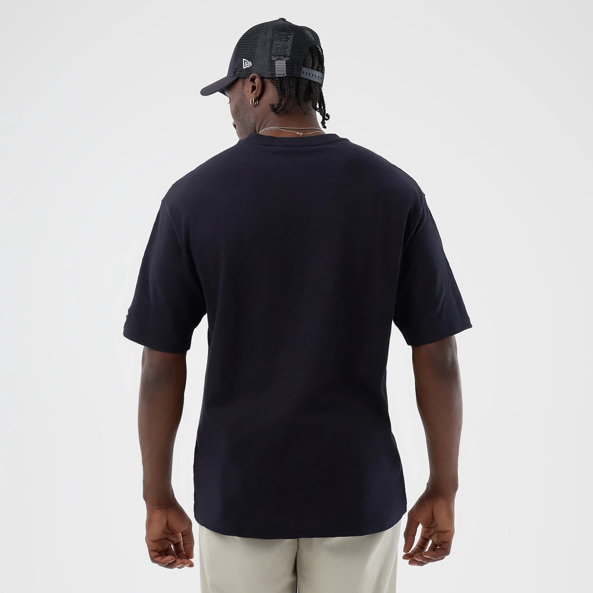New Era LA Dodgers MLB Slub Navy Oversized T-Shirt, back view on a model wearing a black cap, showing the plain navy back design with short sleeves and a relaxed fit that hangs loosely over light-coloured trousers against a neutral background.