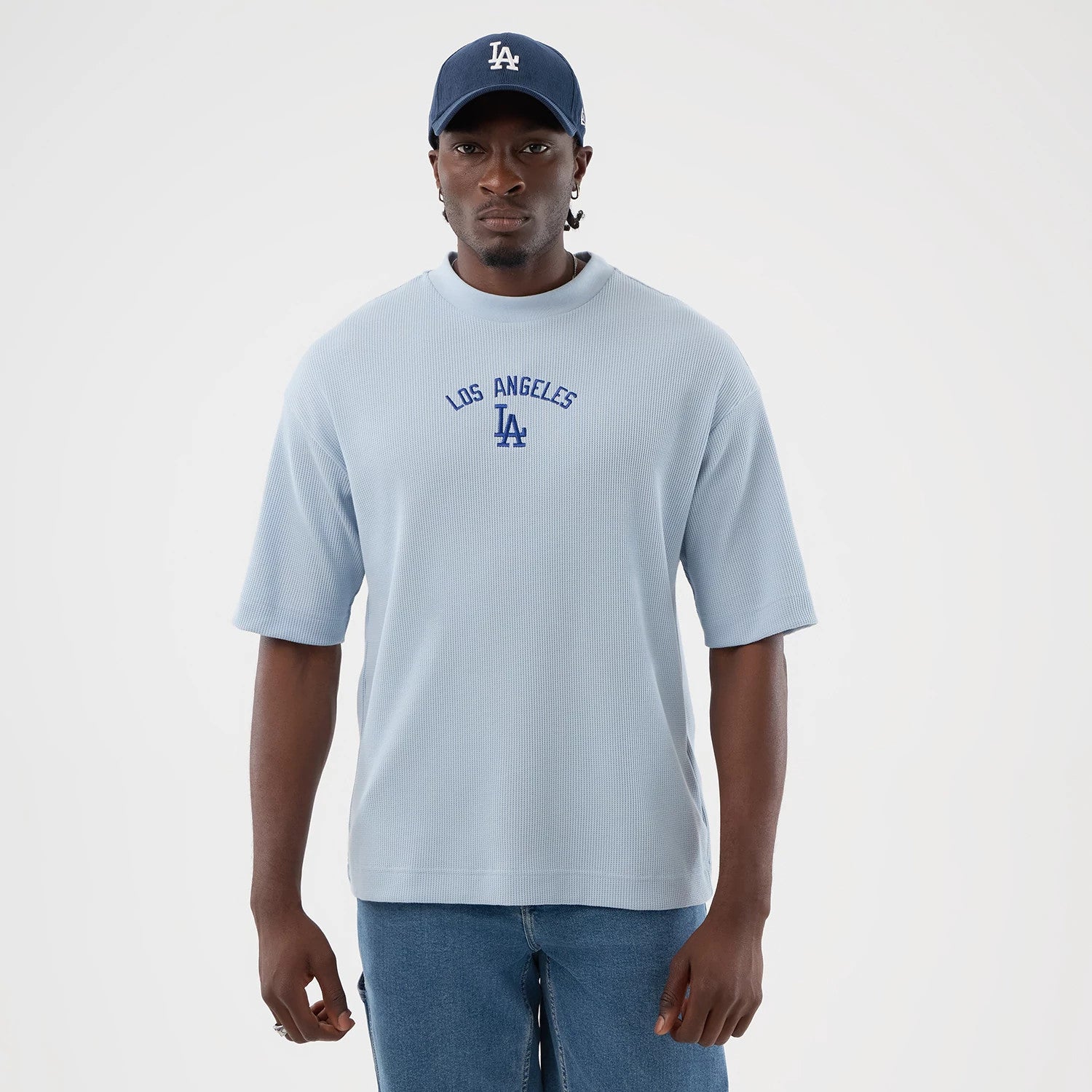 New Era LA Dodgers MLB Waffle Pastel Blue T-Shirt, front view on-model showing the short-sleeved pastel blue top with an embroidered Los Angeles and LA logo in blue centred on the chest, paired with denim jeans and a blue cap for a coordinated look.