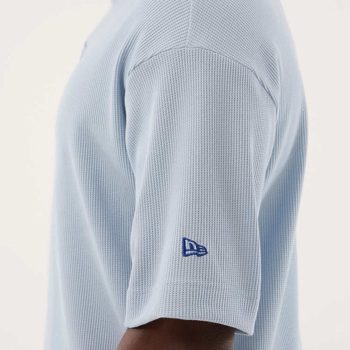 New Era LA Dodgers MLB Waffle Pastel Blue T-Shirt, side view showing the textured waffle pattern on the light blue fabric, with a navy blue embroidered New Era logo near the cuff on the short sleeve.