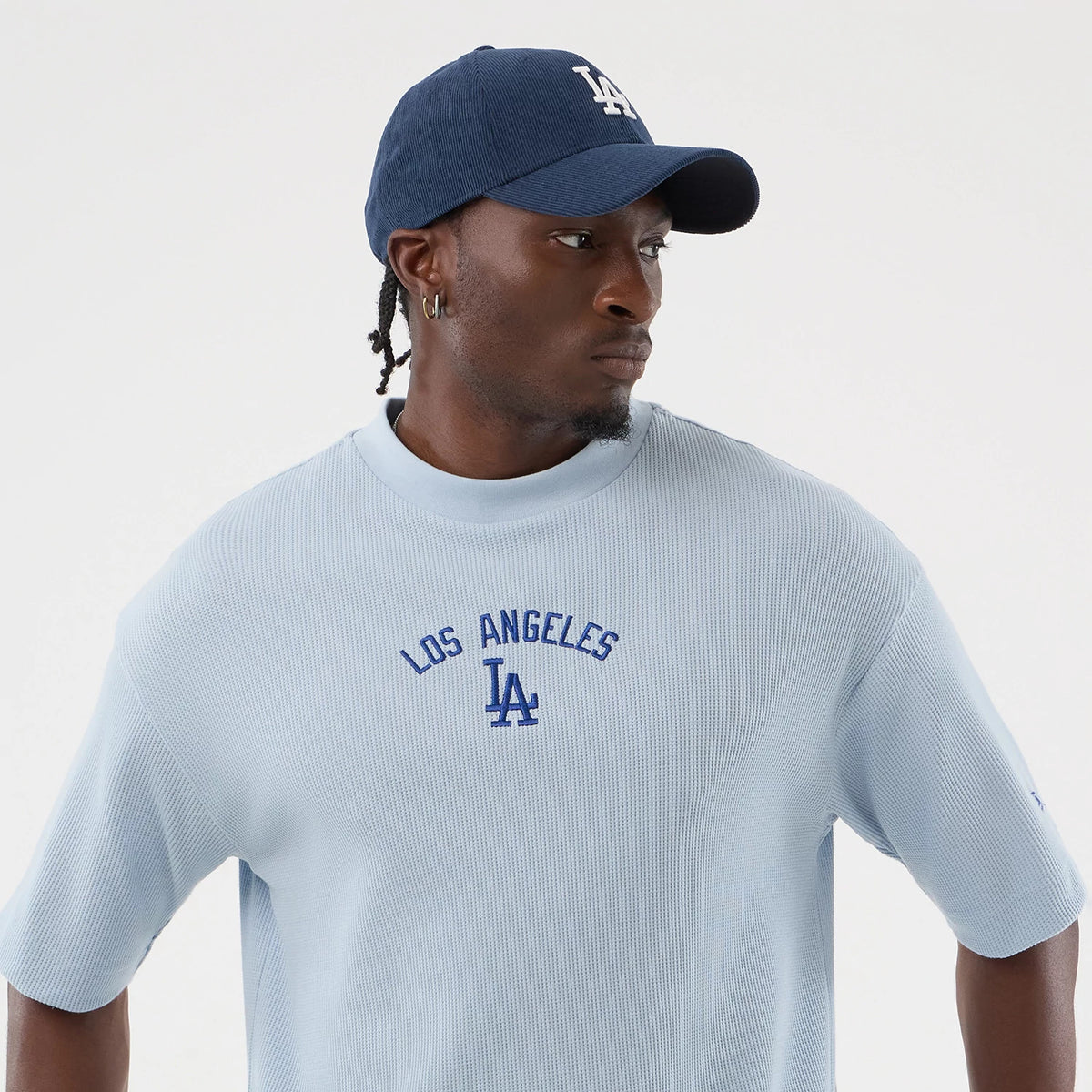 New Era LA Dodgers MLB Waffle Pastel Blue T-Shirt, front view on a model also wearing a navy cap, featuring an embroidered Los Angeles lettering and LA logo in blue on the chest, with relaxed short sleeves and a ribbed crew neckline.