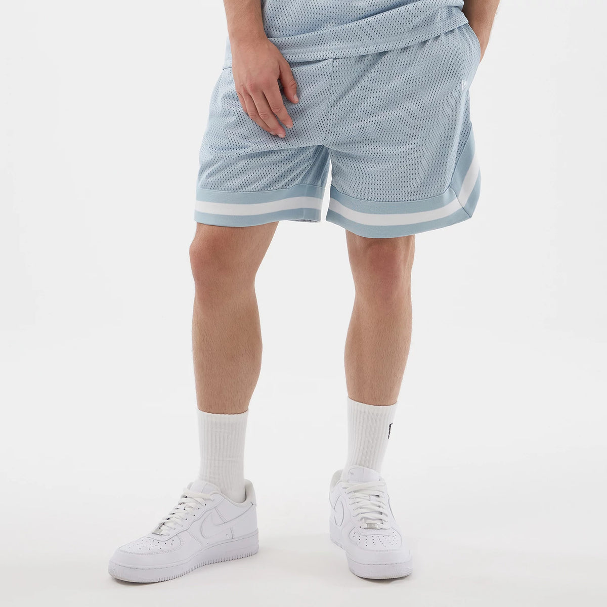 New Era Mesh Pastel Blue Oversized Shorts, front view on a model showcasing the relaxed fit with a patterned mesh texture, white striped trim along the hem, an elasticated waistband, and a raised New Era logo on the left leg.