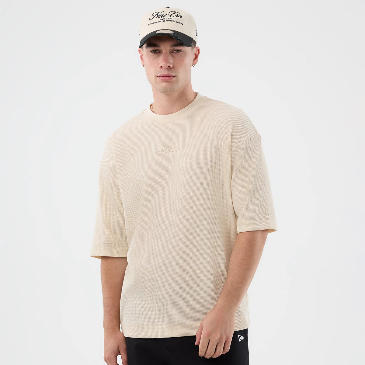 New Era Waffle Light Beige T-Shirt, front view on-model showing the relaxed fit with half sleeves, a embroidered logo on the chest, and styled with a light beige New Era cap featuring an embroidered script on the crown.