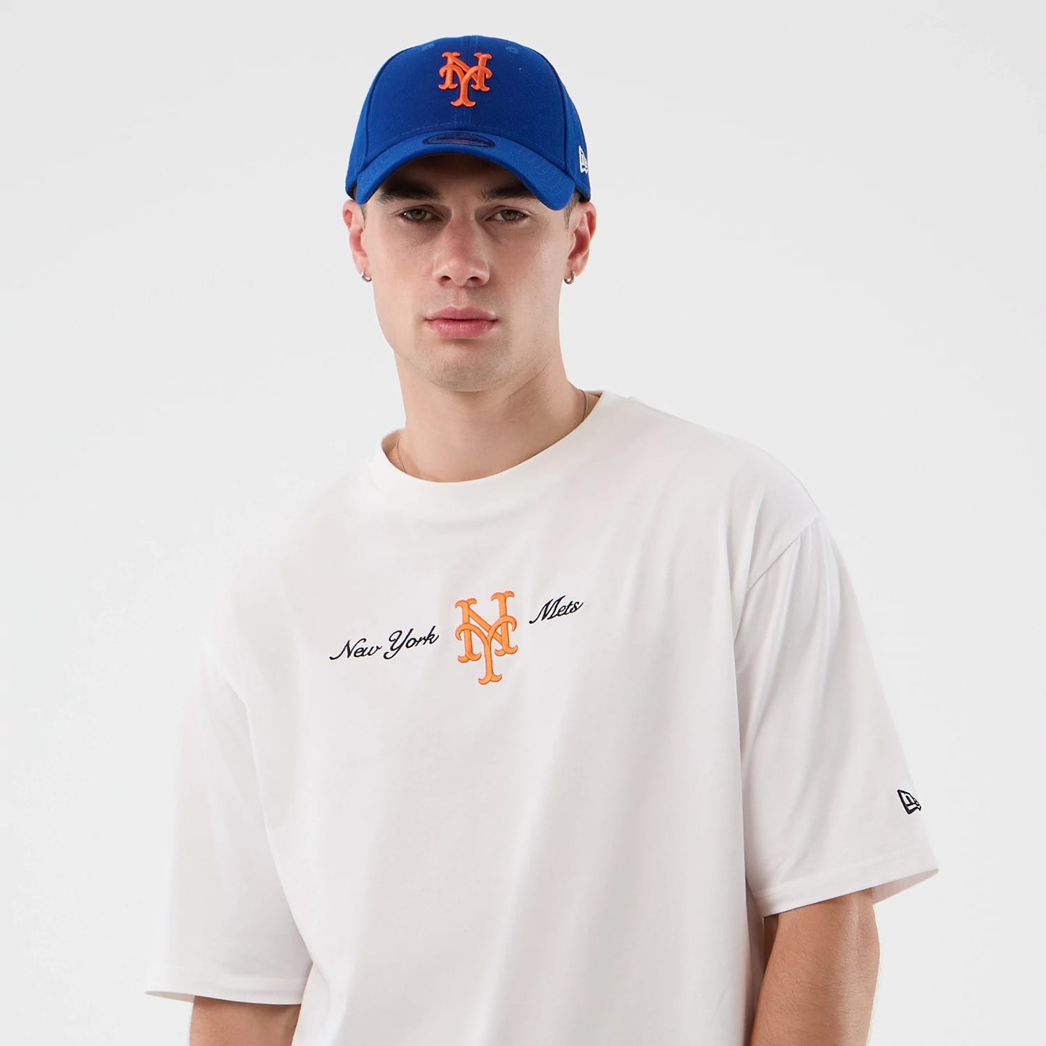 New Era New York Mets MLB Script White Oversized T-Shirt, front view on-model showing the New York Mets lettering and orange embroidered logo at the centre of the chest, along with the New Era flag embroidered on the left sleeve.