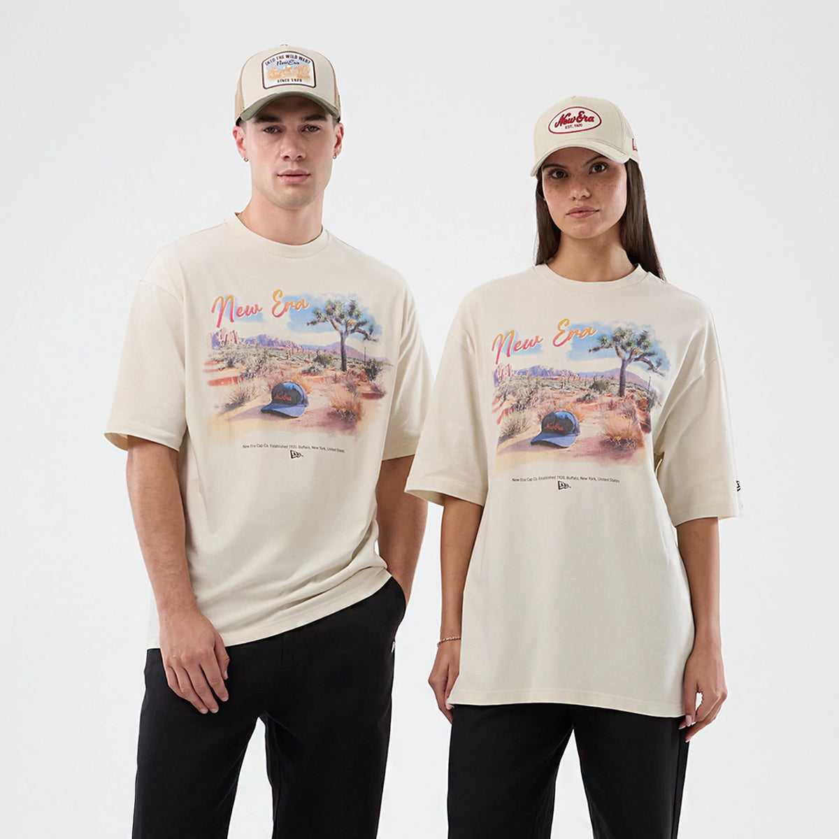 New Era Dessert Graphic Light Beige Oversized T-Shirt, front view on models, each wearing the shirt with a printed desert landscape graphic in colours, New Era scripted across the chest, and a small embroidered logo at the hem.
