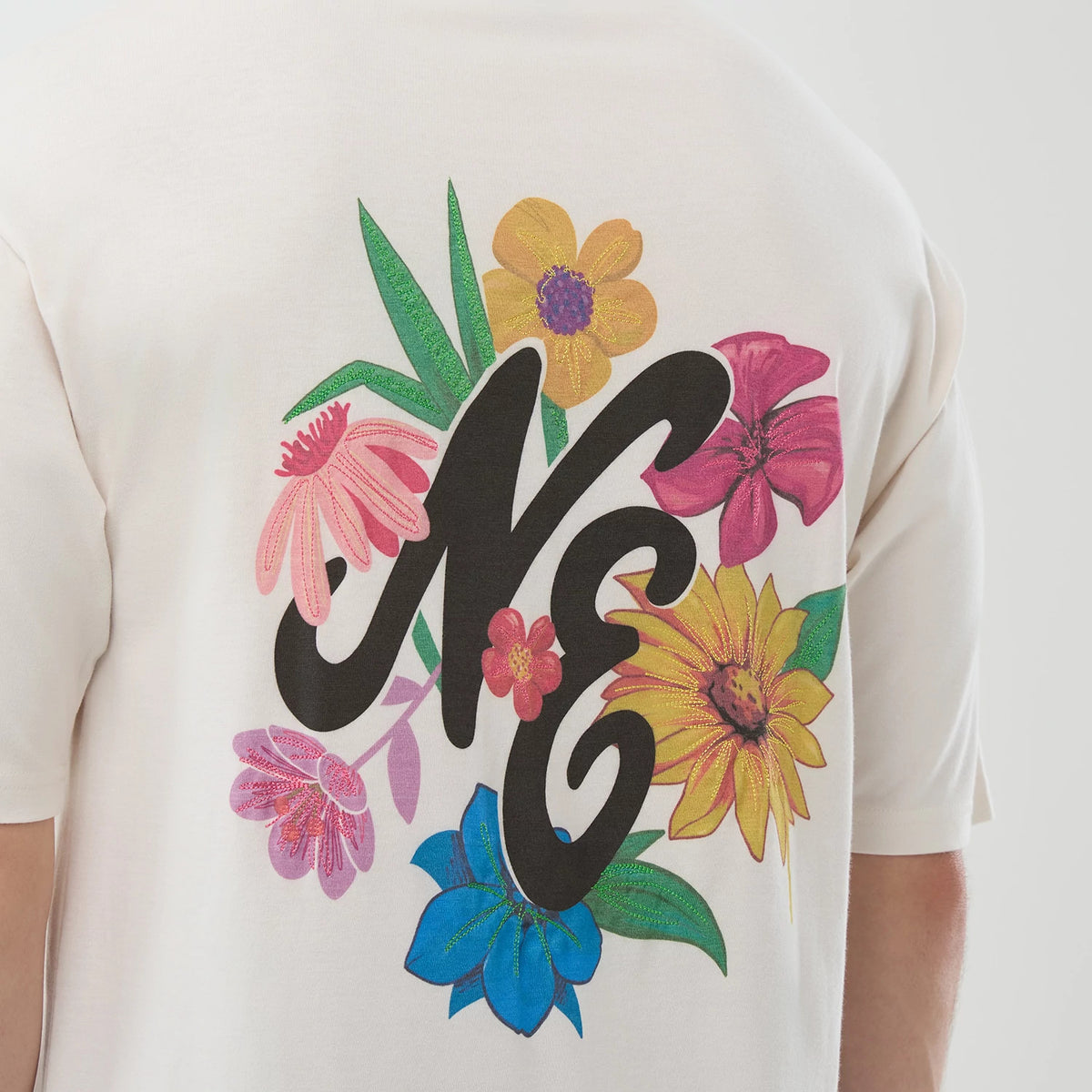 New Era Floral Graphic Open White Oversized T-Shirt, back view showing a large printed NE logo surrounded by flower graphics, including pink, yellow, blue, and purple flowers with green leaves, set across the upper back.