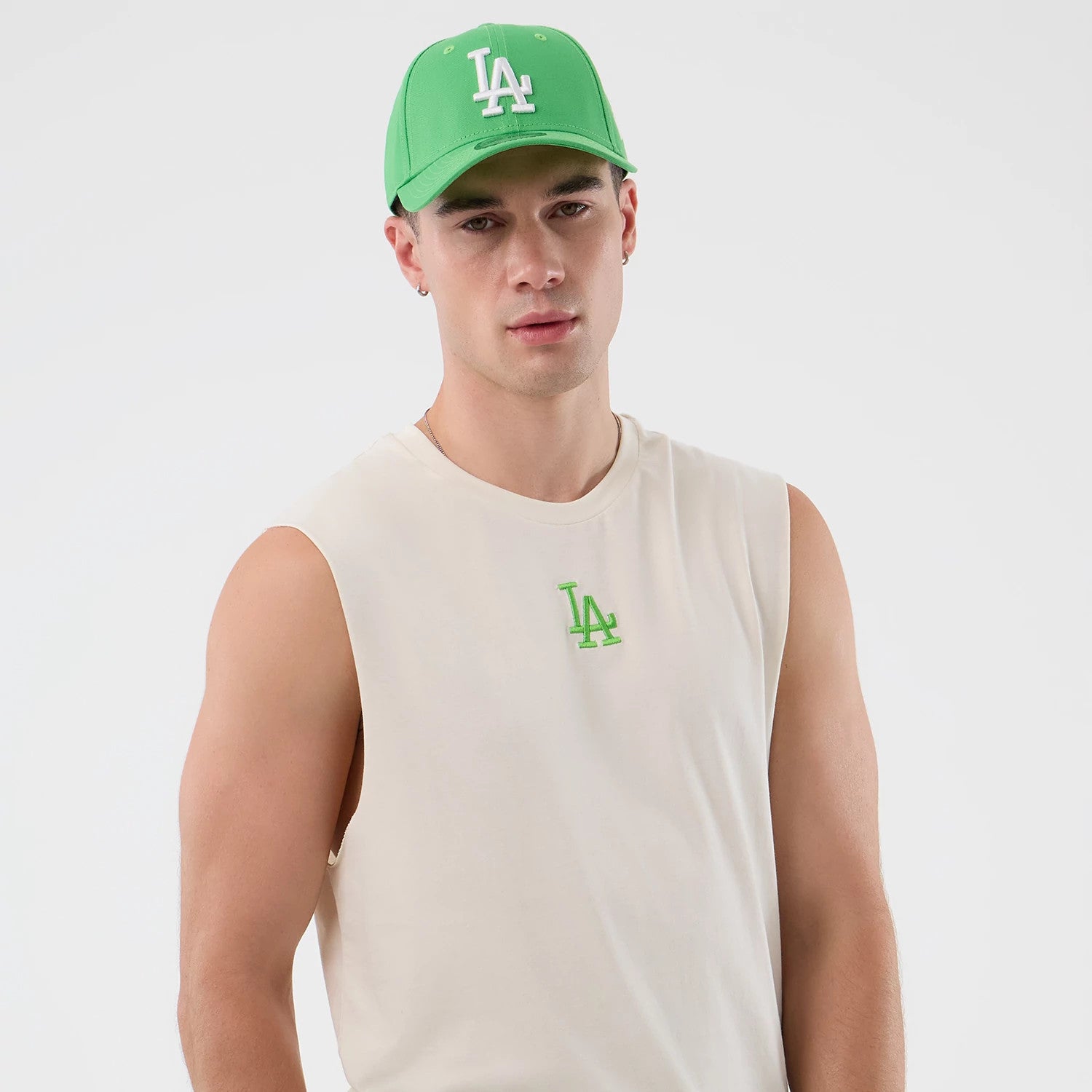 New Era LA Dodgers MLB League Essential Open White Vest, front view on a model wearing a green New Era cap, featuring a small green embroidered LA logo on the left chest, sleeveless design for a relaxed and casual fit.
