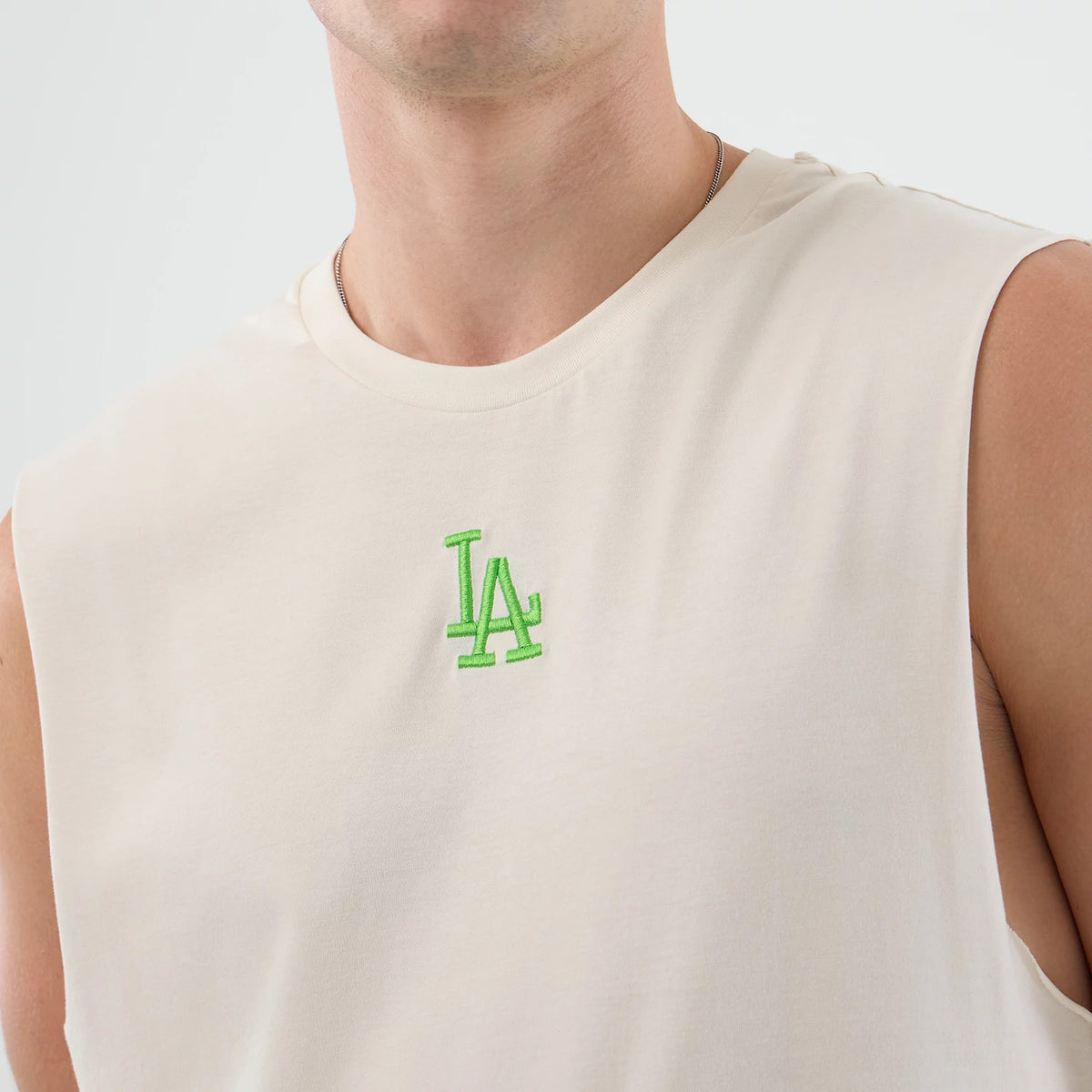 New Era LA Dodgers MLB League Essential Open White Vest, front view on a model with a light cream colour, featuring a small neon green embroidered LA logo on the left chest and sleeveless arm openings.