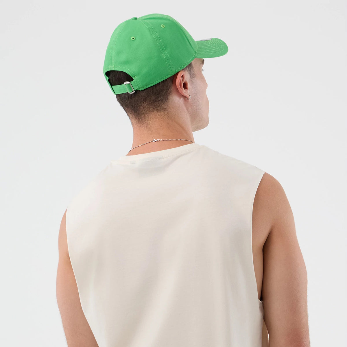 New Era LA Dodgers MLB League Essential Open White Vest, on-model rear view showing sleeveless design, loose fit and light fabric, paired with a green cap featuring an adjustable back strap with buckle.