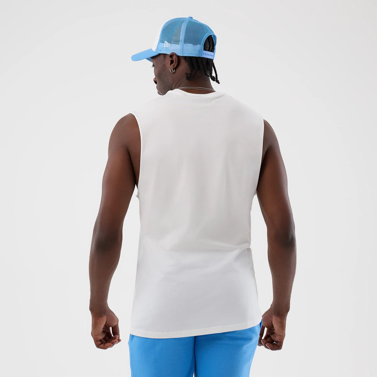 New Era New York Yankees MLB League Essential White Vest, back view on a model with a light blue mesh-back cap, showing the sleeveless white fabric, a relaxed fit unembellished back, and a straight hem resting above blue shorts.
