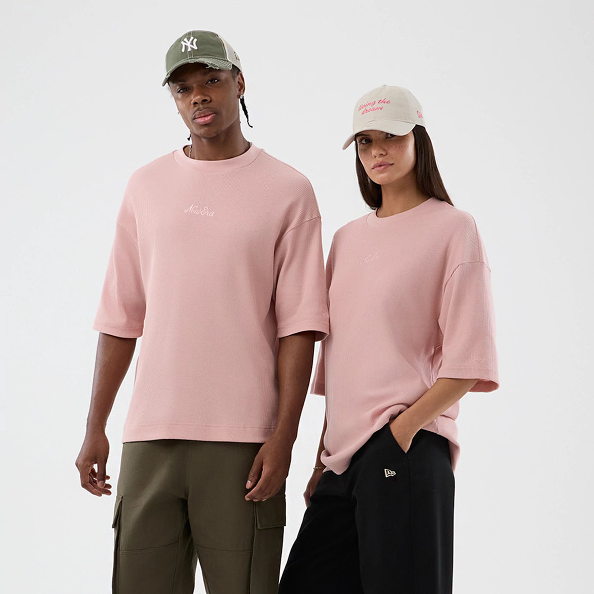 New Era Waffle Pastel Pink T-Shirt, front view on-model showing an embroidered New Era logo at the centre chest, oversized fit with short sleeves, paired with contrasting trousers, and stitching details near the hems.