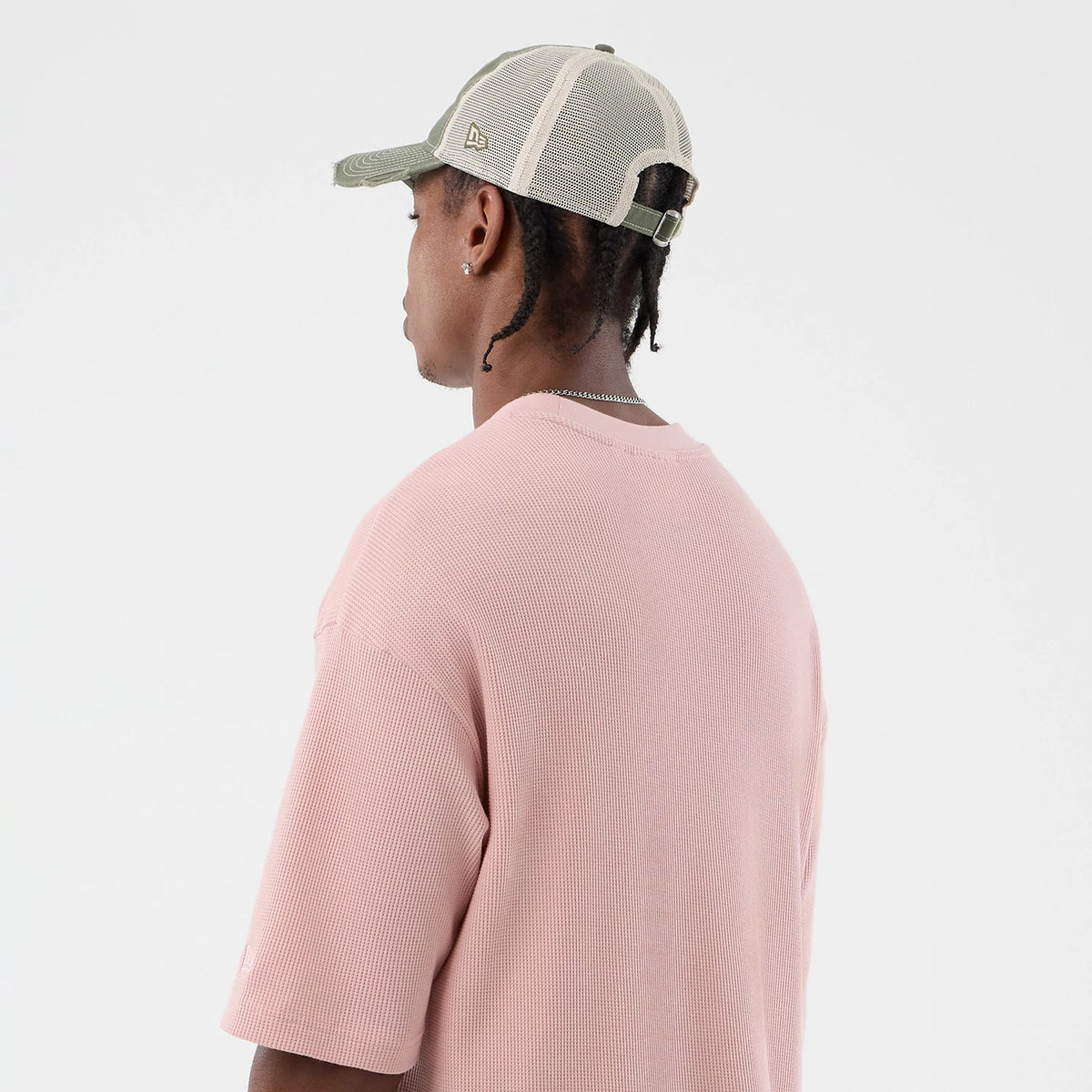 New Era Waffle Pastel Pink T-Shirt, back view on a model showing the textured waffle design and relaxed fit, paired with a mesh cap having a small embroidered New Era logo on the side, creating a casual, coordinated look.